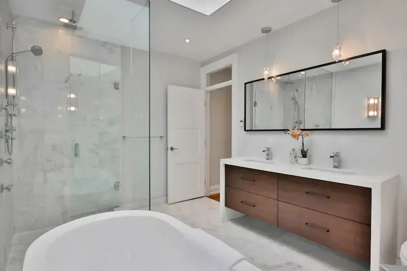 Modern bathroom with a wall-mounted mirror, a gray vanity with a sink, a white toilet, and a glass-enclosed shower featuring a rainfall showerhead.